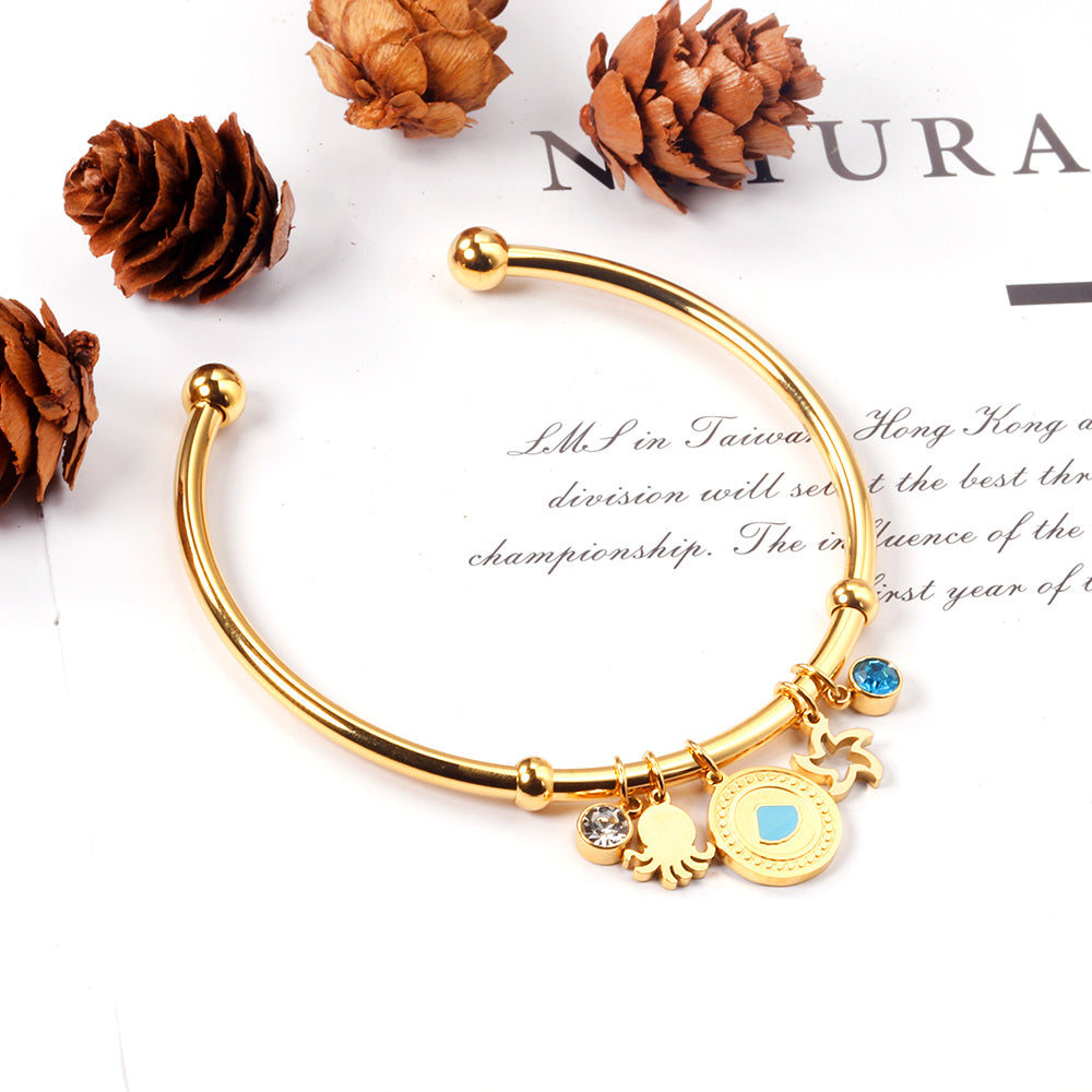 Gold bangle with two diamonds of different colors and a charm with a scallop on the door of the discus. asonjewelry